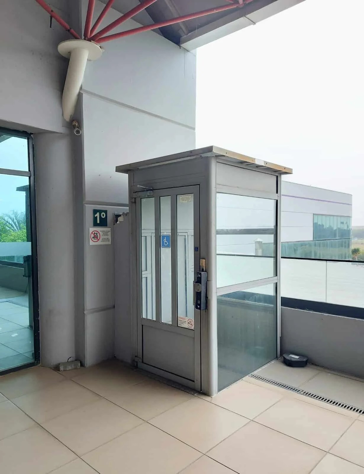 A segunda imagem mostra o elevador no piso superior. Ao lado do elevador, uma placa indica que se está no primeiro andar.