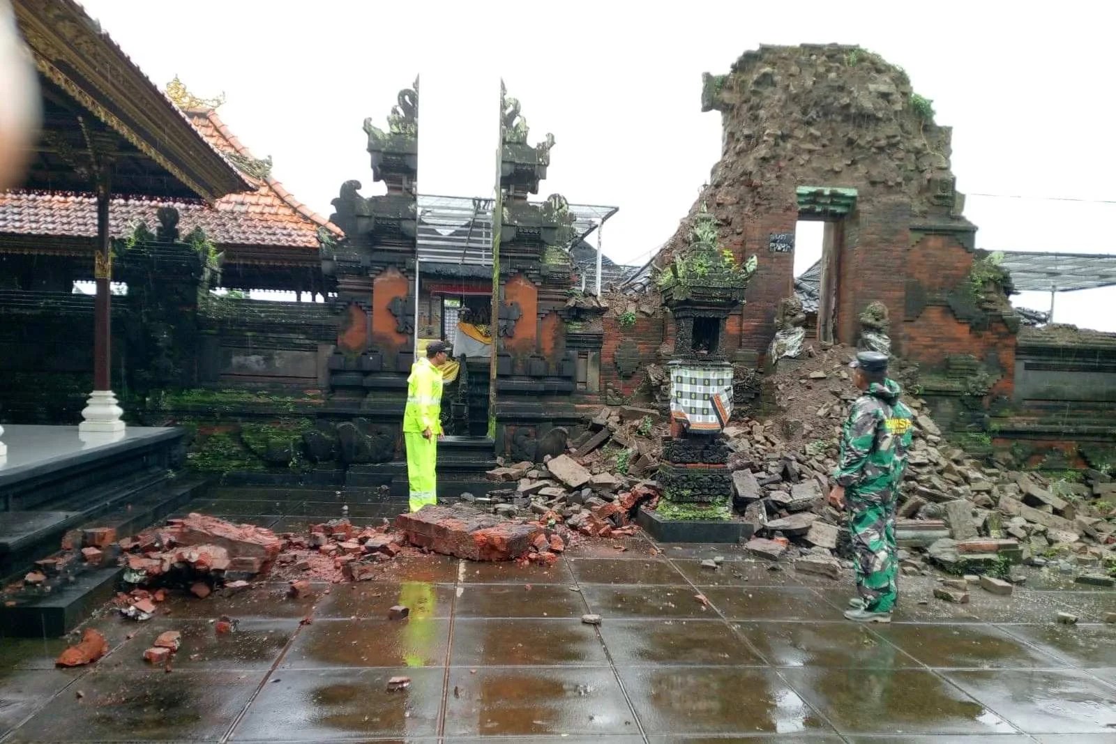 Bhabinkamtibmas dan warga mengecek kondisi Candi Bentar Pura Kayangan Dalem Kauh yang rubuh akibat hujan lebat.