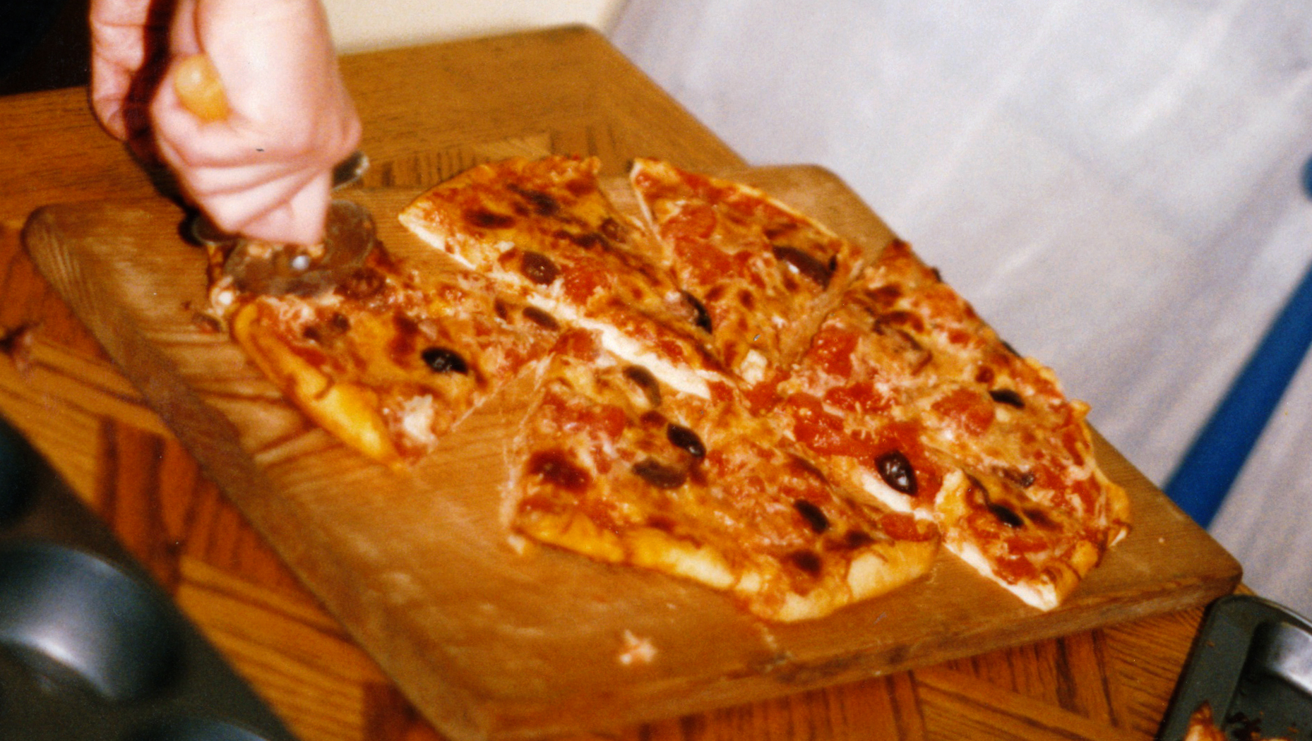Rolling pizza wheel cutting a thin pizza into triangle slices on a board
