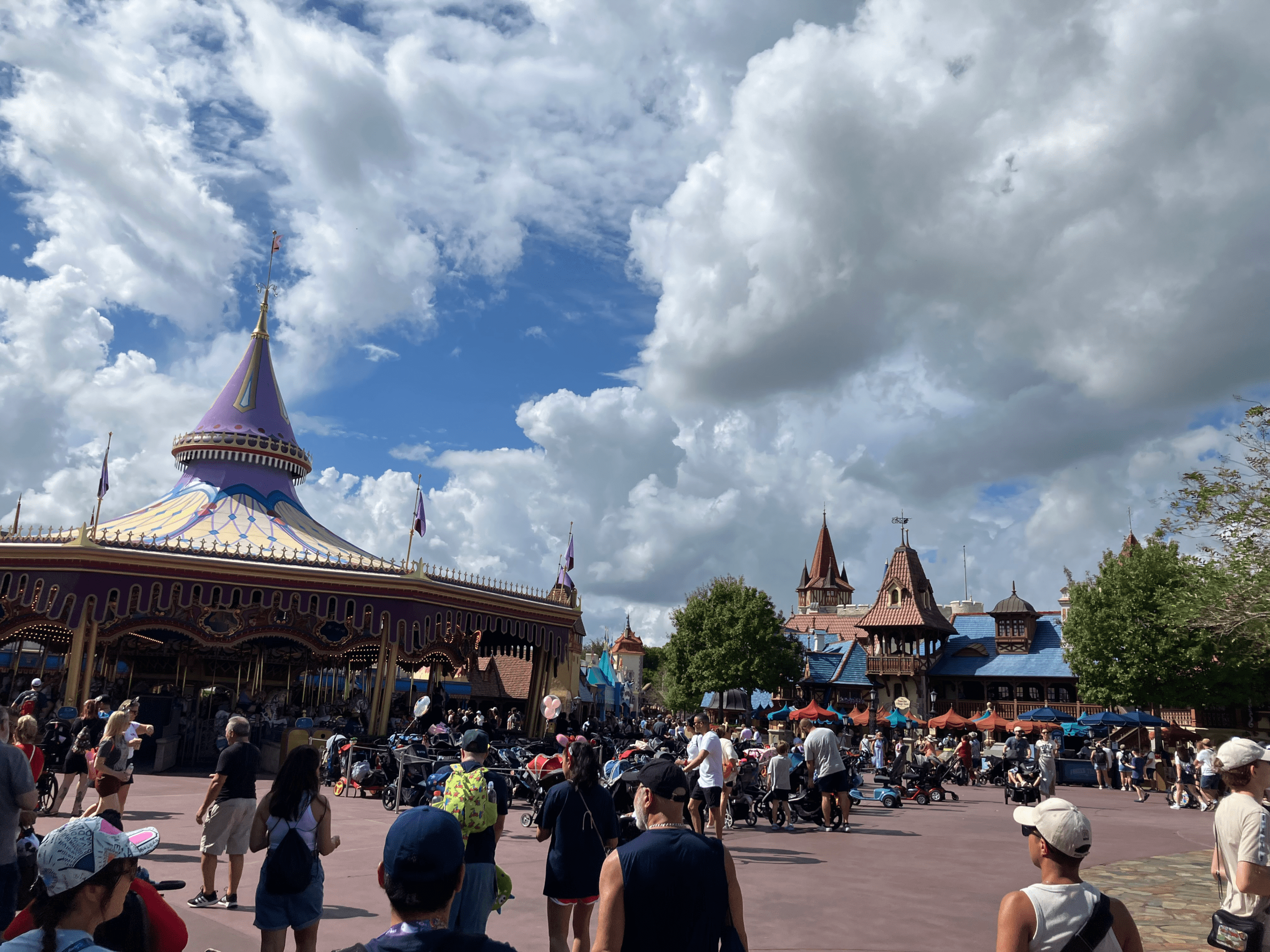 A crowd of people outside of a carousel on a partly cloudy day.