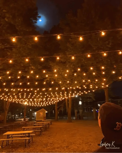 The Salem Commons underneath tons of orange string lights with a full moon overhead at night, with no one there 