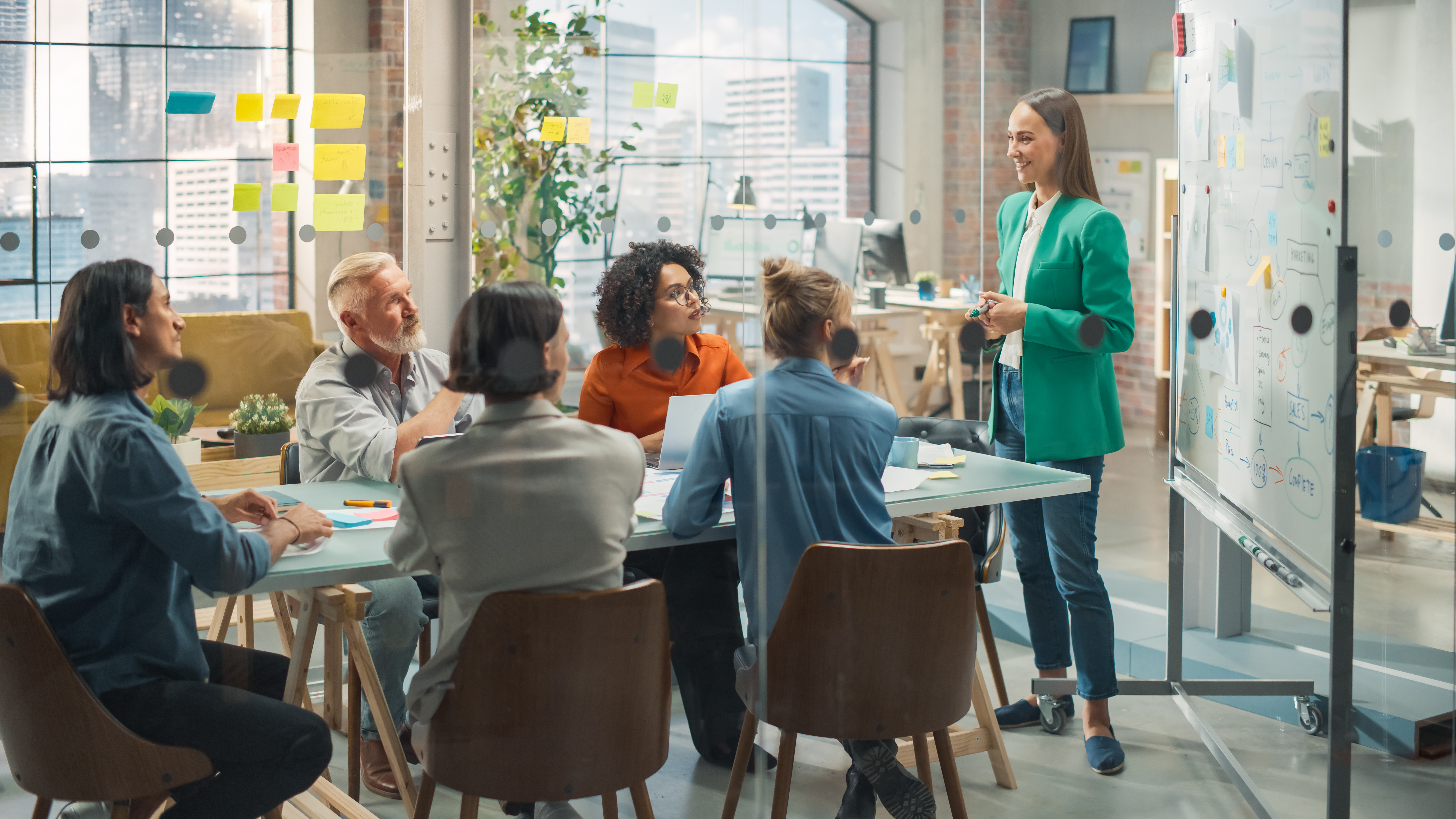 Team meeting in a modern office, discussing strategies with a woman presenting and a whiteboard displaying notes, reflecting collaboration in public relations initiatives.