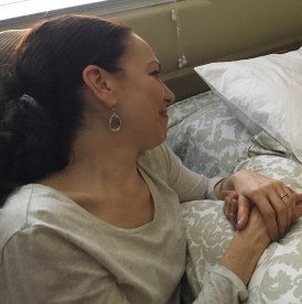 Photo of Ginny sitting by her mother's bedside, holding her mother's hand