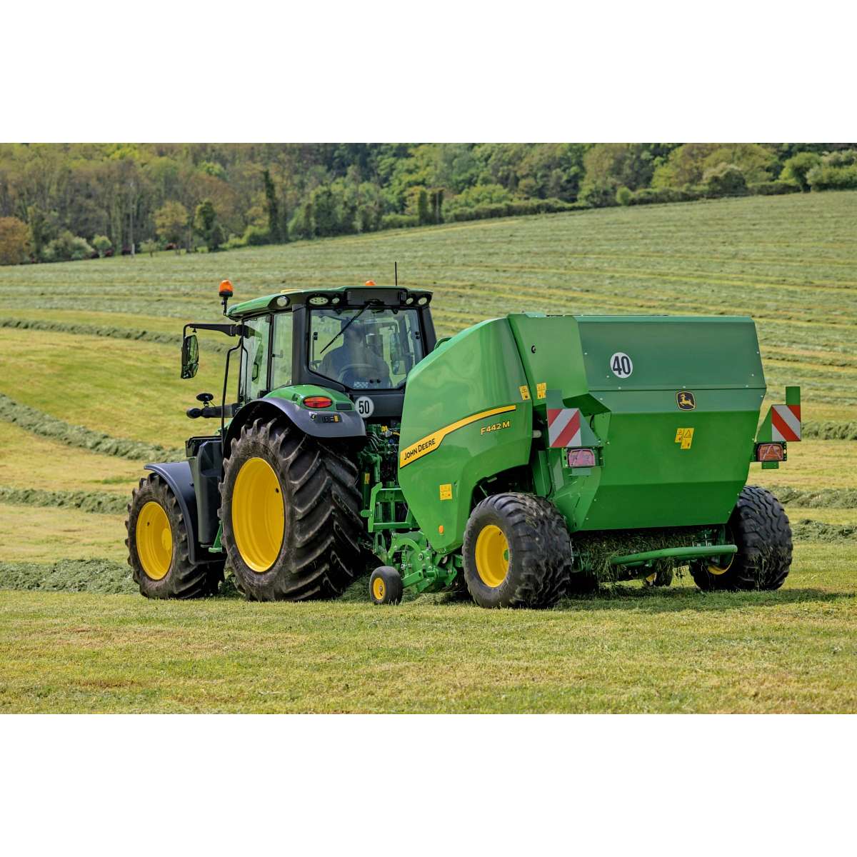Presa de balotat John Deere F442M trasă de un tractor John Deere 6M pe un câmp deluros cu iarbă