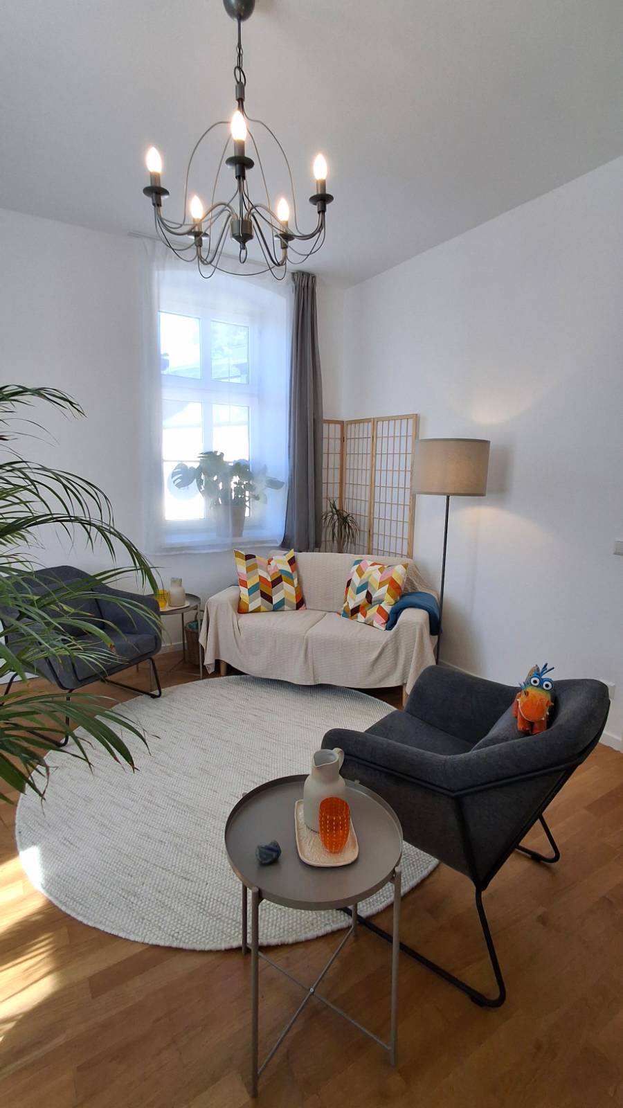 Das Foto zeigt den Beratungsraum von Irina Langers Praxis: 2 graue Stühle mit je 1 Beistelltisch, 1 kleine beigefarbene Couch, Pflanzen