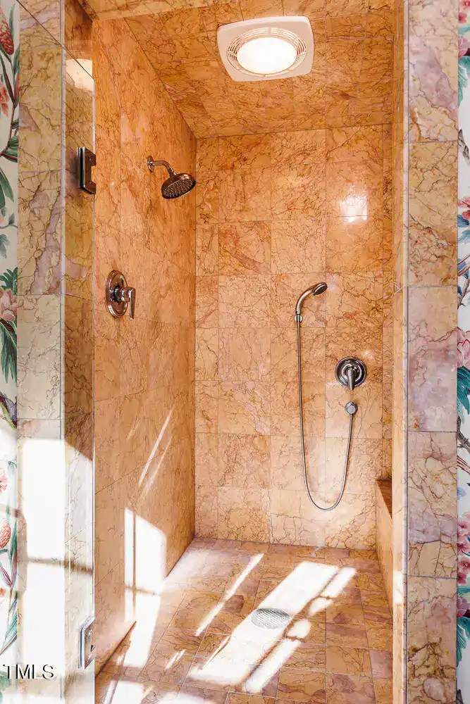 Polished marble shower with dual showerheads and natural sunlight, showcasing elegant bathroom design and luxurious finishes.
