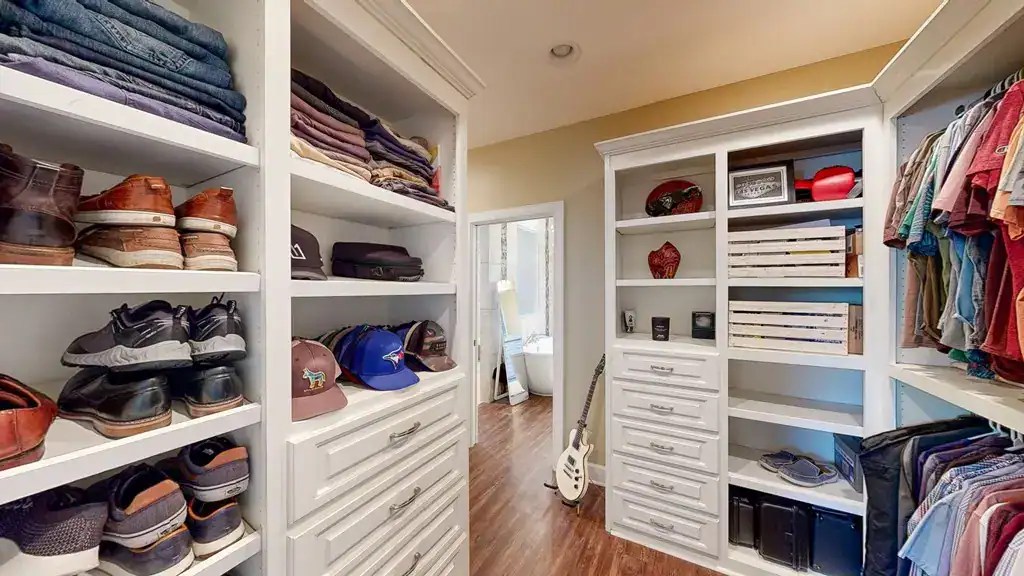 Organized walk-in closet with white shelving and drawers showcasing shoes, hats, folded clothes, and accessories for stylish wardrobe storage.
