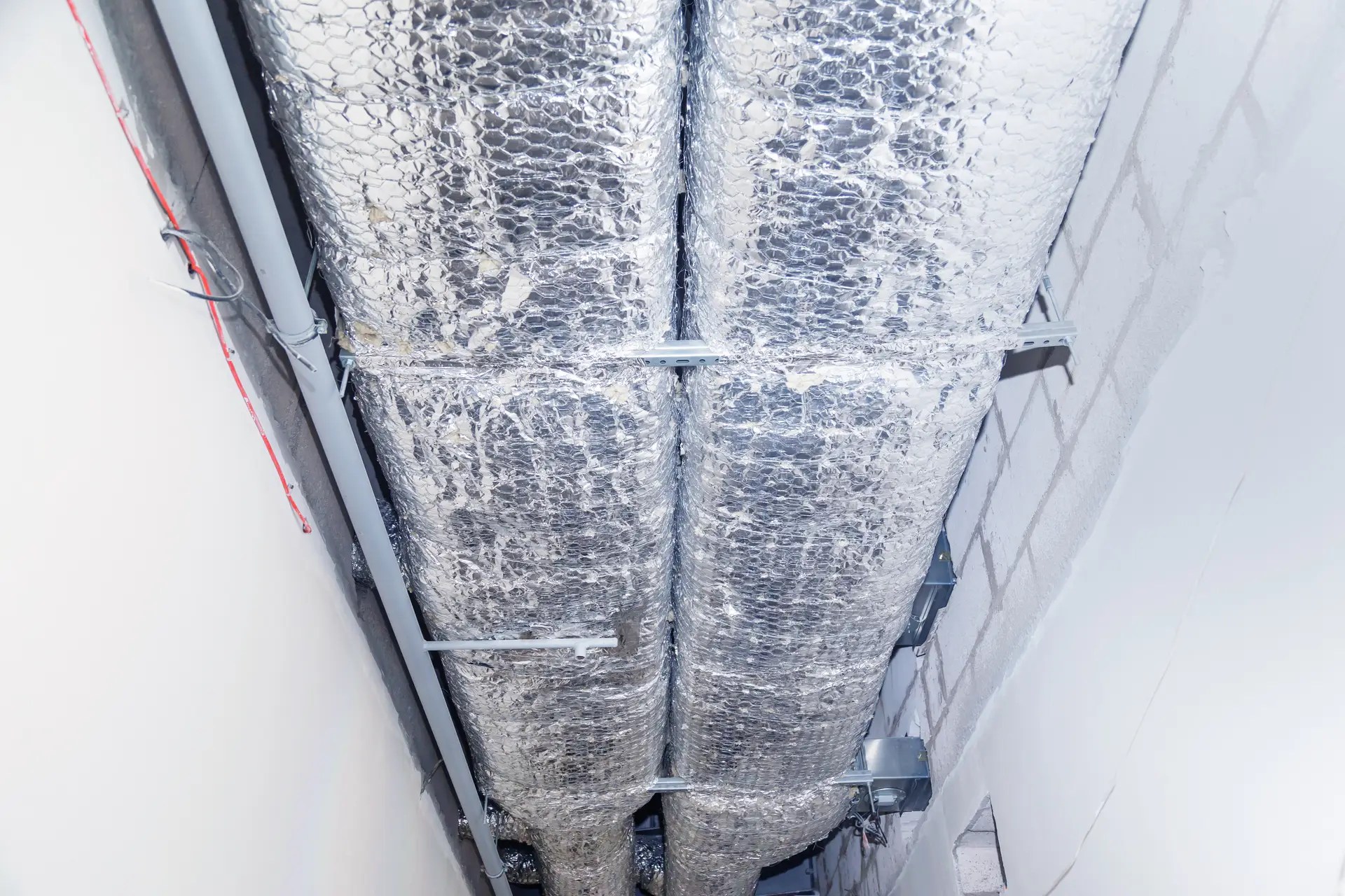 HVAC Duct Cleaning, Ventilation pipes in silver insulation material hanging from the ceiling inside new building.