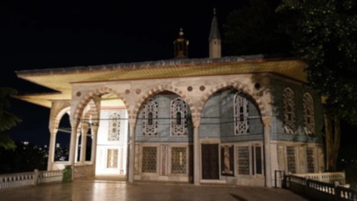 An arched, tiled building with a golden roof at night.
