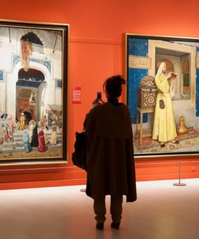 A person views two historic paintings in a gallery.