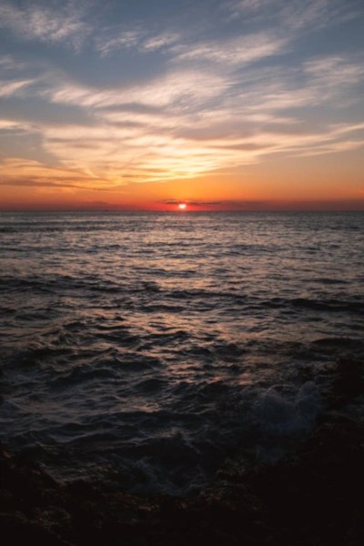 A dramatic sunset over the sea, with a bright orange sun and dark, rolling waves.