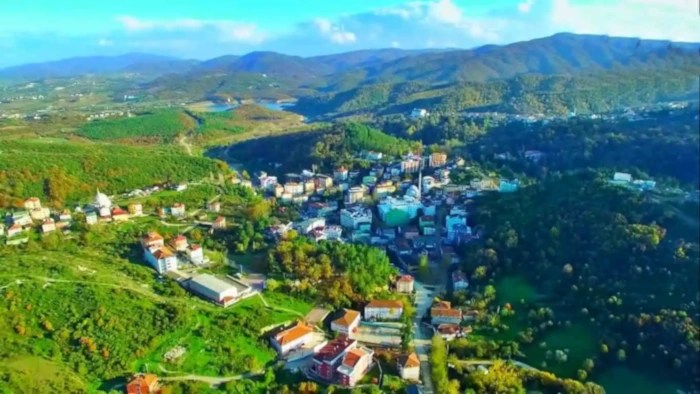 An aerial view of a town nestled in a valley, surrounded by lush green hills and a reservoir in the distance.