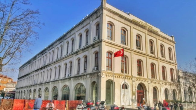 The historic stone facade of the Beyazıt State Library in Istanbul, with its distinctive Ottoman domes and arches.