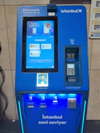 A modern blue Istanbul Biletmatik ticket and top-up machine with a touchscreen, card slot, and glowing LED lights, located in a metro or station setting.