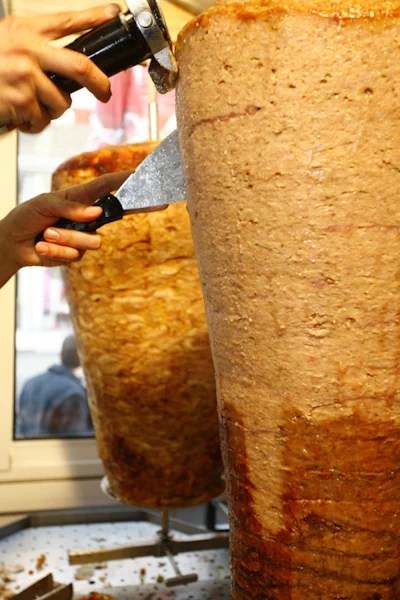 Factory-made döner on a vertical spit, with a person slicing pieces.