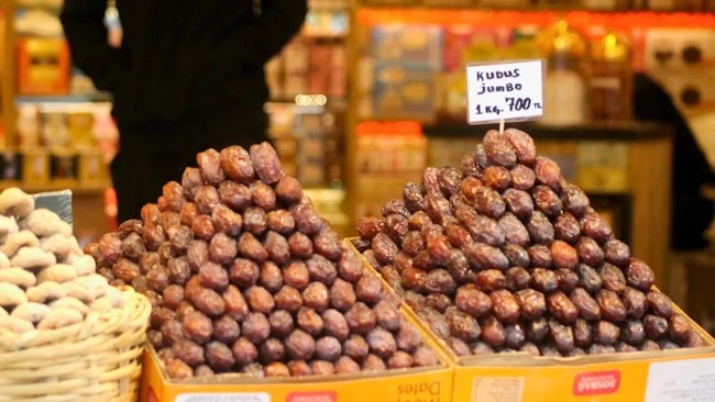 Two pyramids of Kudus dates displayed in a small shop, showcasing the glossy, rich-brown fruit.