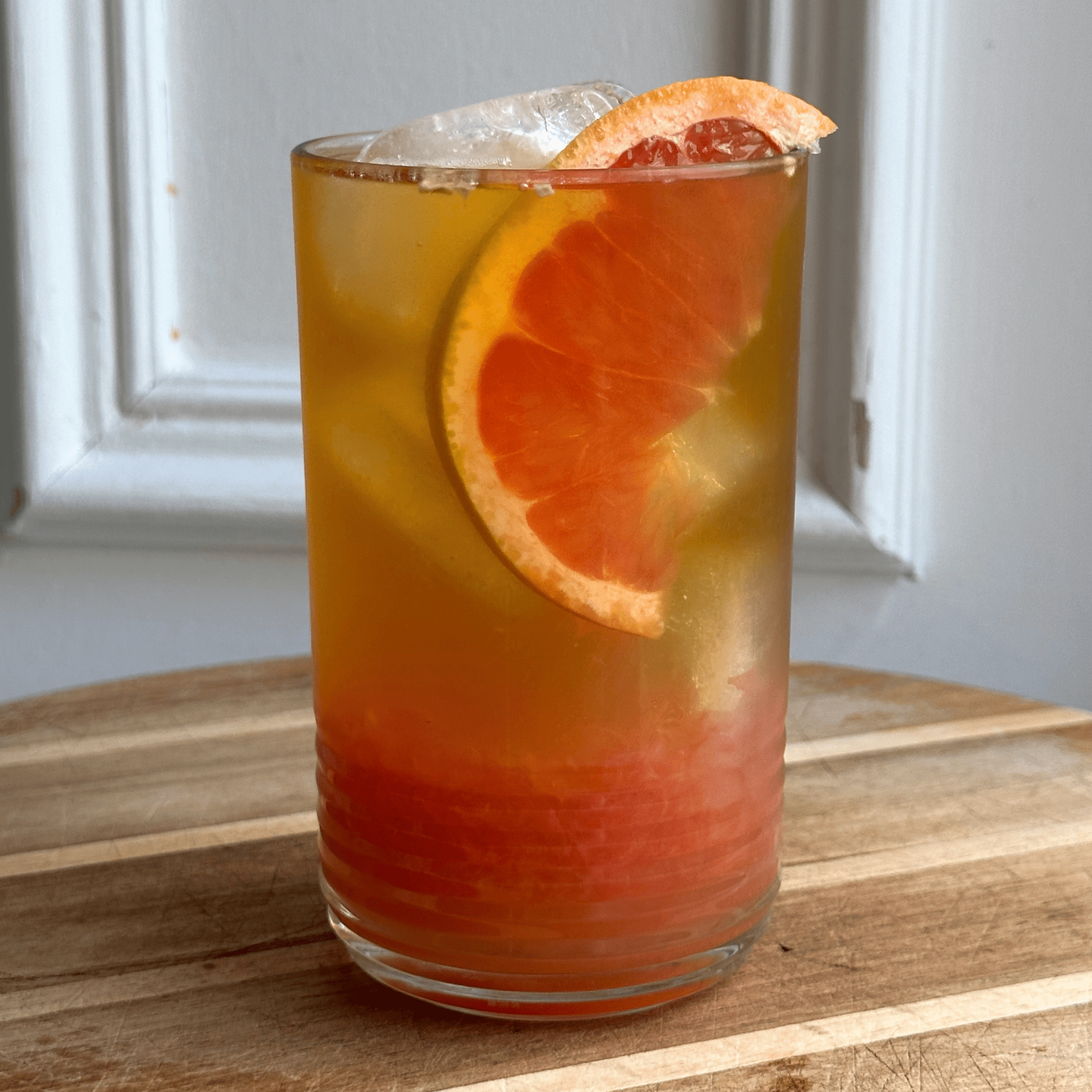 a glass of ice tea with grapefruit just and pulp at the bottom. Ice in the glass with a golden tea colour, and a wedge of grapefruit place in the glass