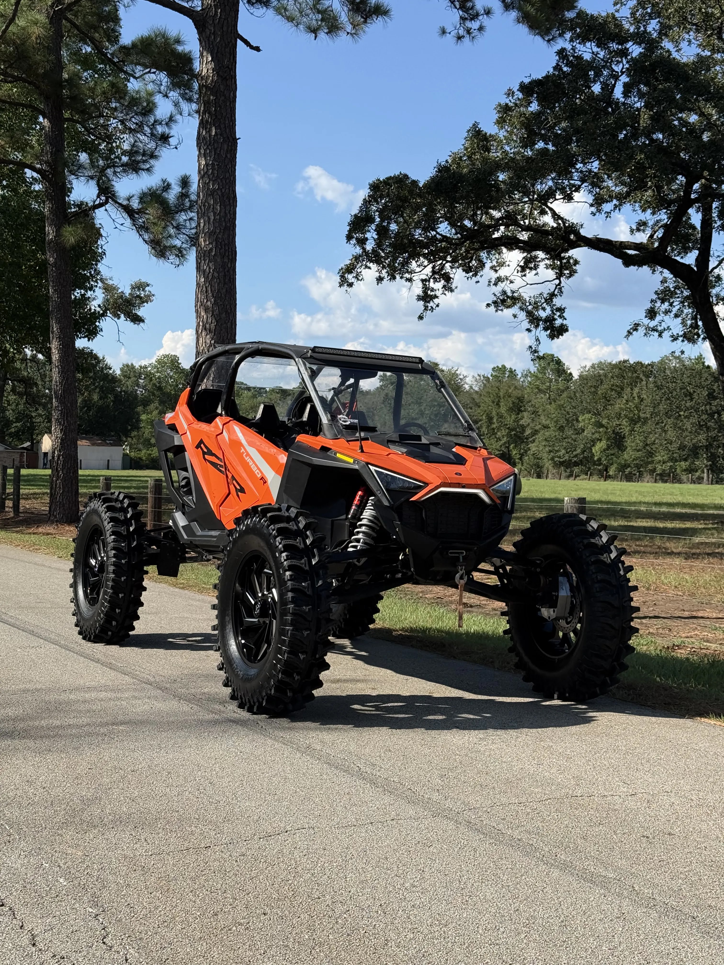 Orange Polaris RZR custom build from the opposite front angle, showing oversized mud tires and raised suspension