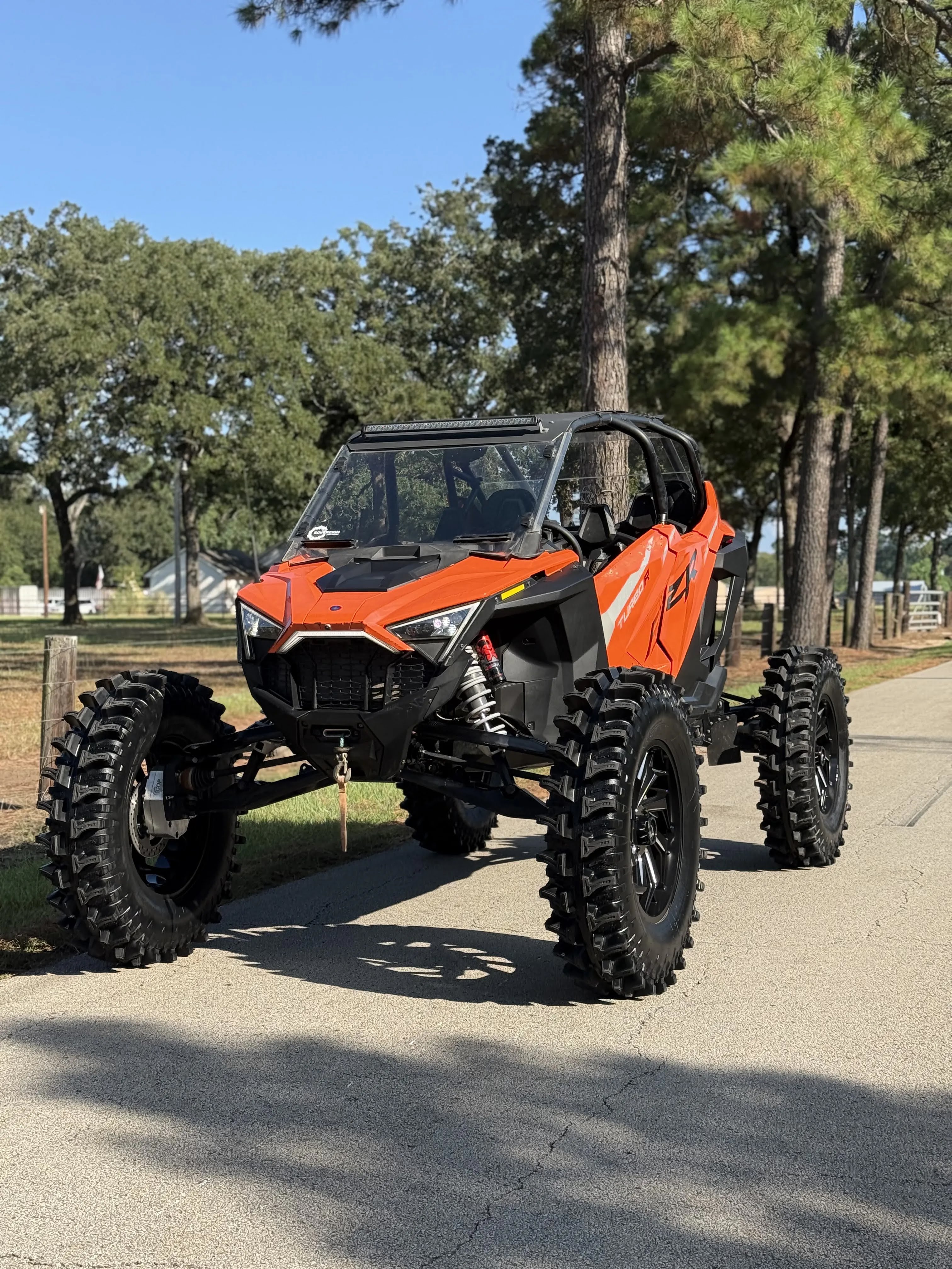 Orange Polaris RZR custom build with oversized mud tires, raised suspension, windshield and roof light bar