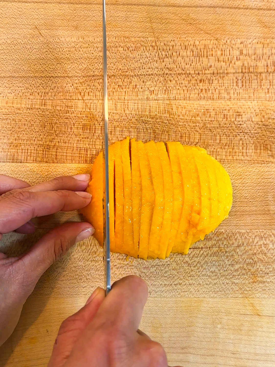 Slicing ripe mango into thin strips on a wooden cutting board
