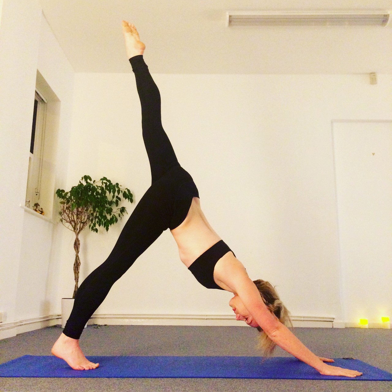 Image shows Jade practising a 3 legged dog yoga pose in a yoga studio in Beeston, Nottingham.