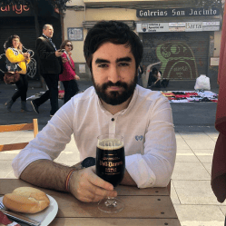 Photo of Jamedi Gwent drinking a beer at a table beside a bustling but pleasant street.