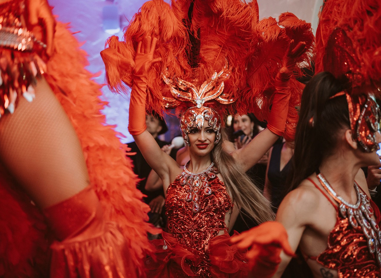 Red showgirl dancer with feathered headpiece performing during Hora Loca at Villa Woodbine Miami wedding.