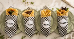 Four assorted Middle Eastern wraps served on green plates, featuring different fillings and wrapped in black-and-white checkered paper with Jasmine branding.