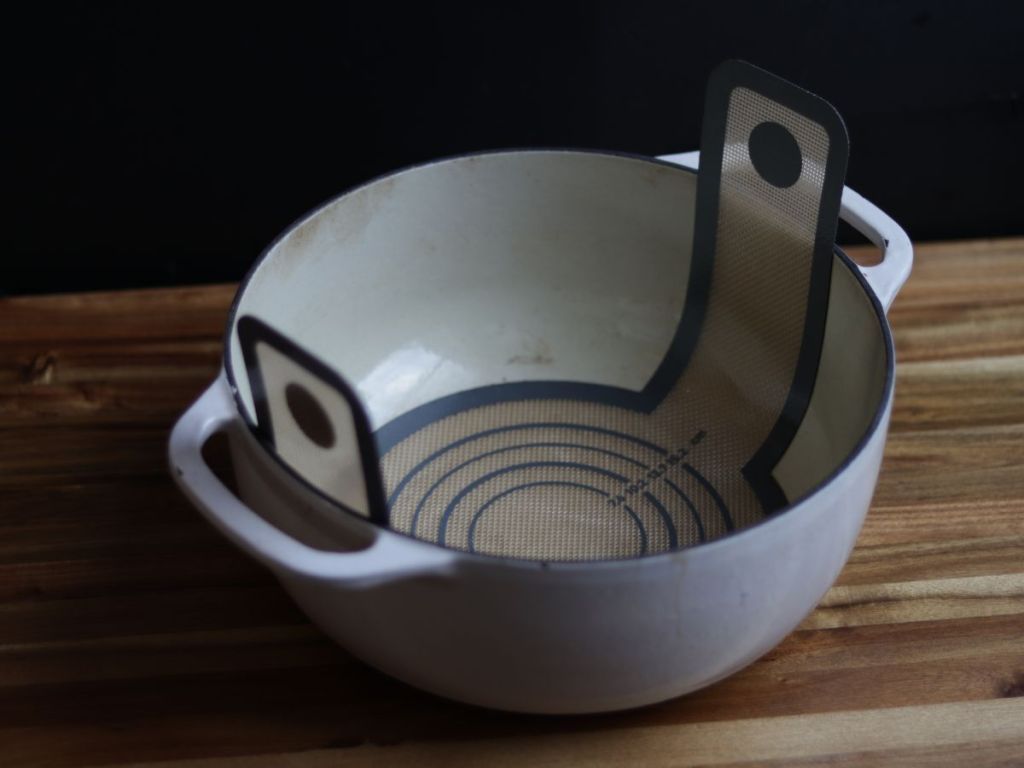 dutch oven with a silicone baking sling sitting on a wooden cutting board