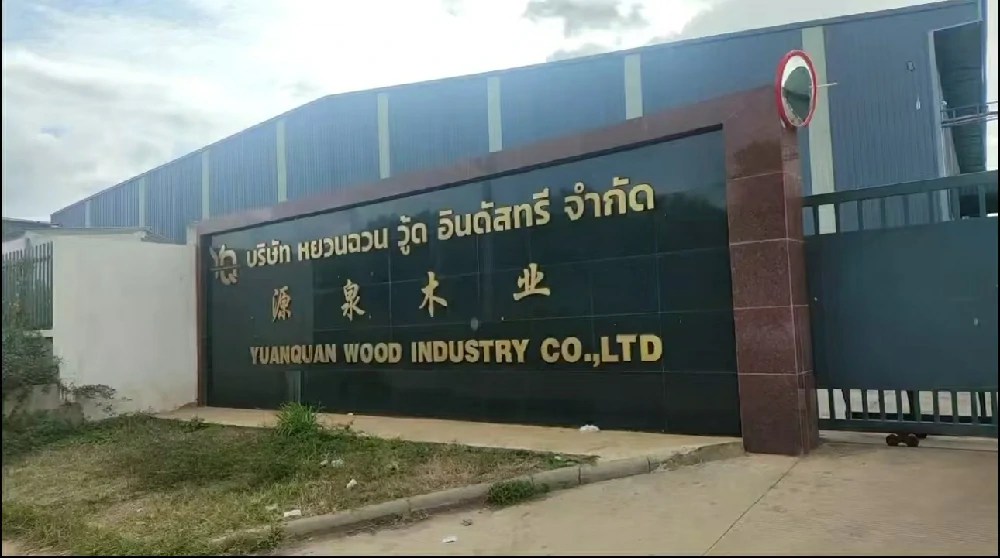 The signage at the factory entrance displays the name “Yuanquan Wood Industry” in Thai, Chinese, and English.