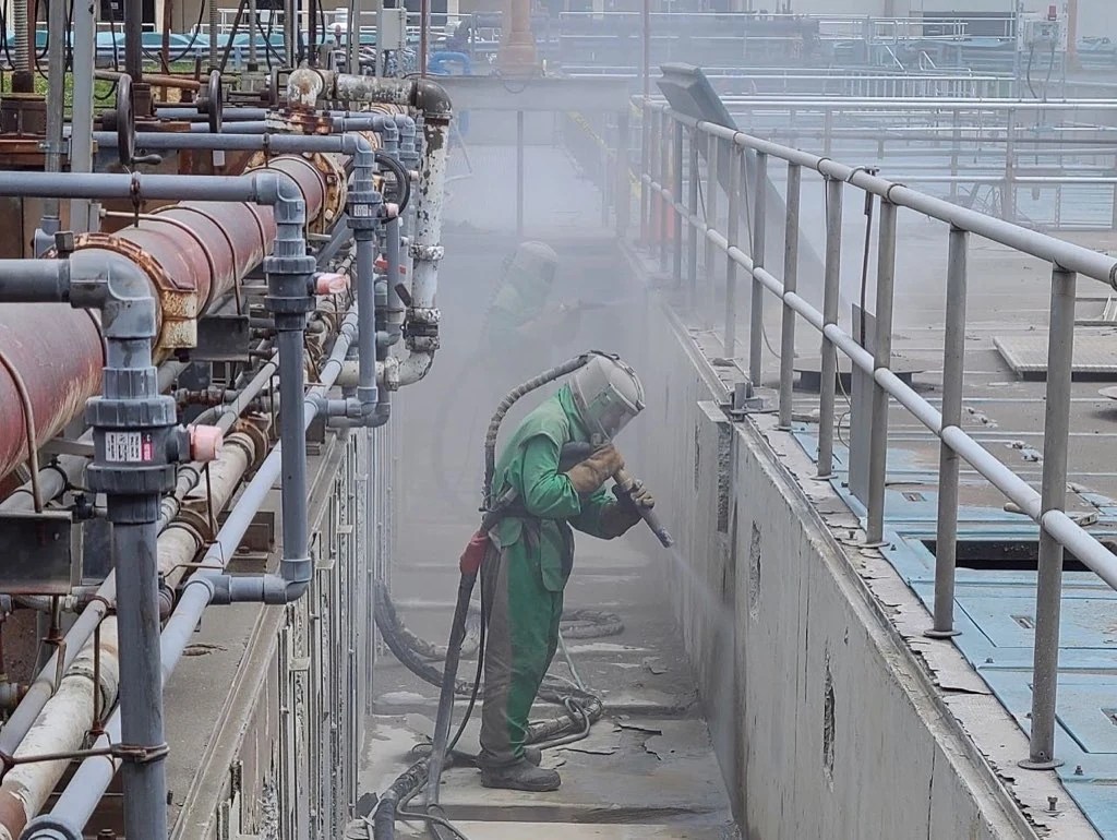 Worker performing media blasting for surface preparation at an industrial facility.