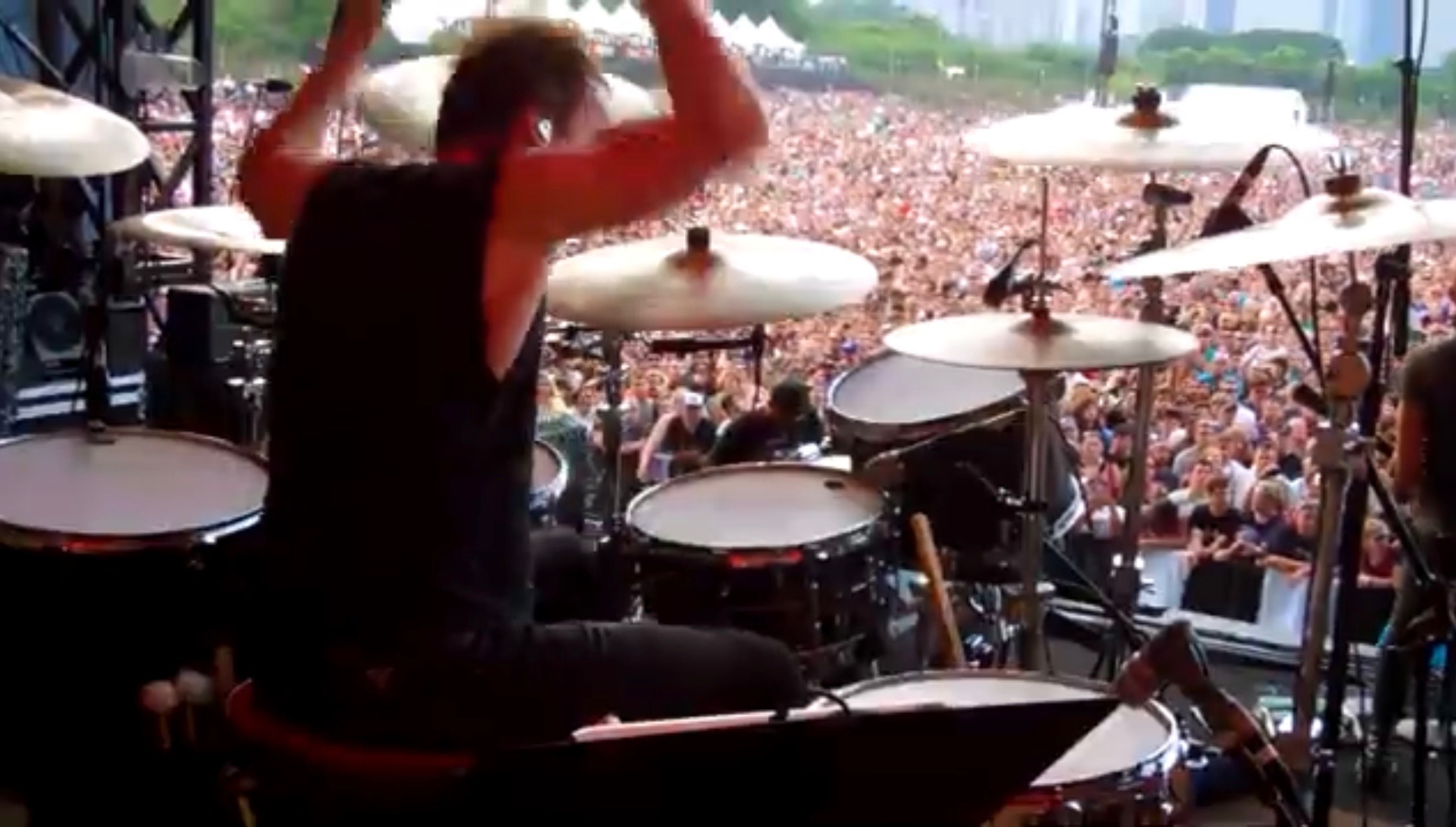 Drummer plays high-energy set on stage before a massive festival crowd, seen from behind the drum kit.