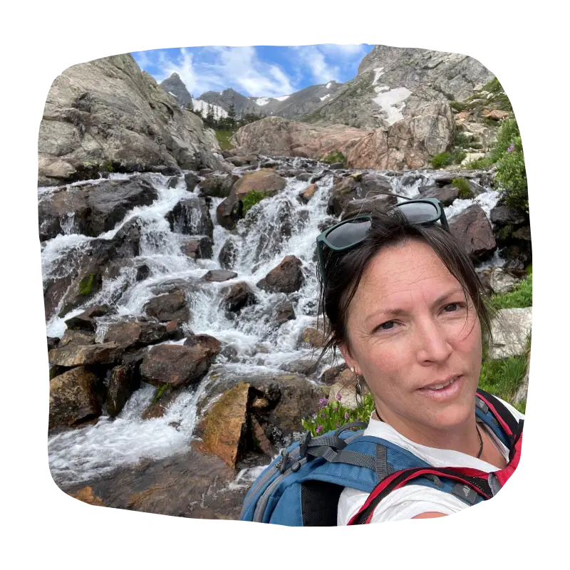 Photo of massage therapist Jennifer Johnson in front of a waterfall while on a mountain hike.