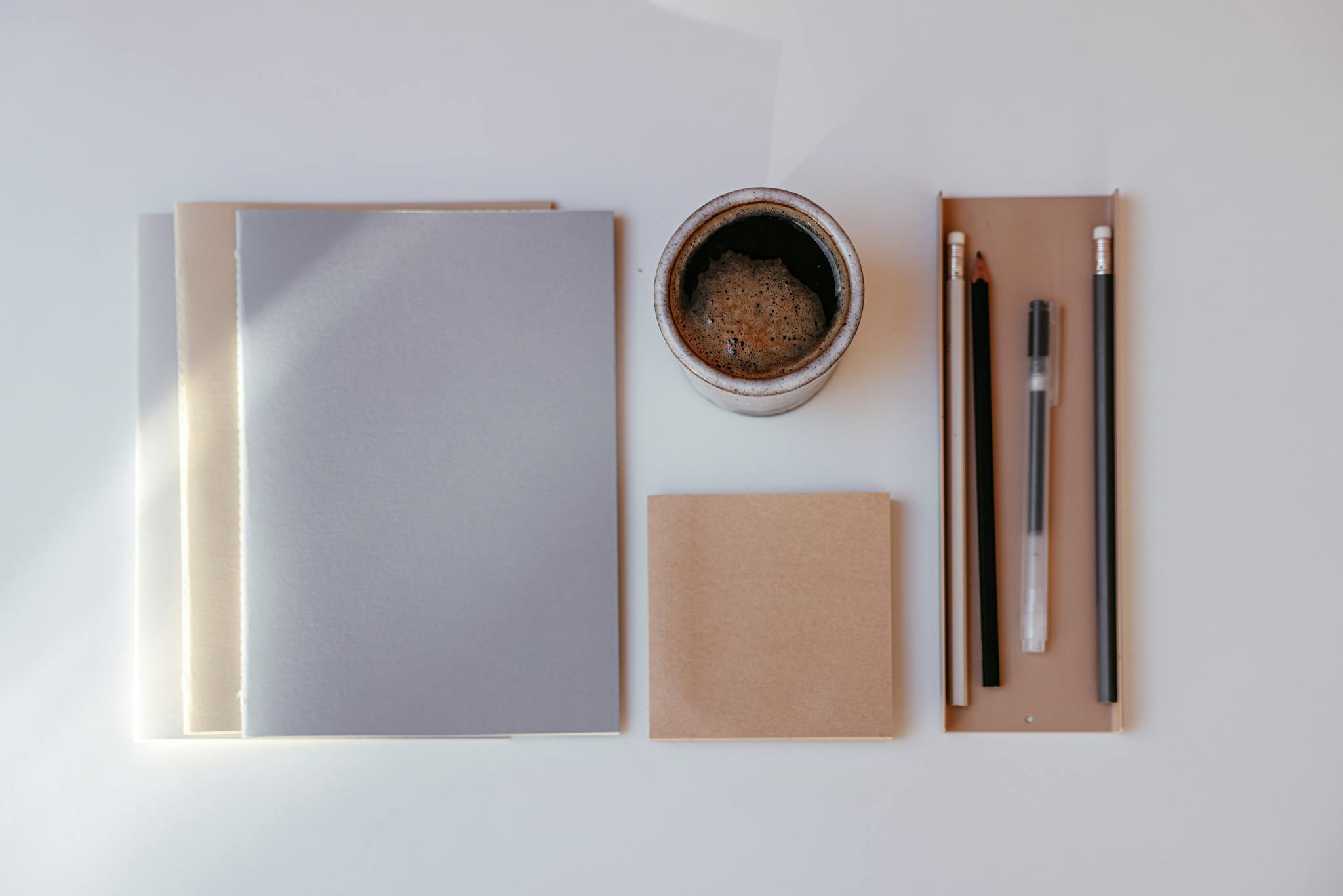 A minimalist arrangement of a coffee cup, notebooks, and stationery on a white background.