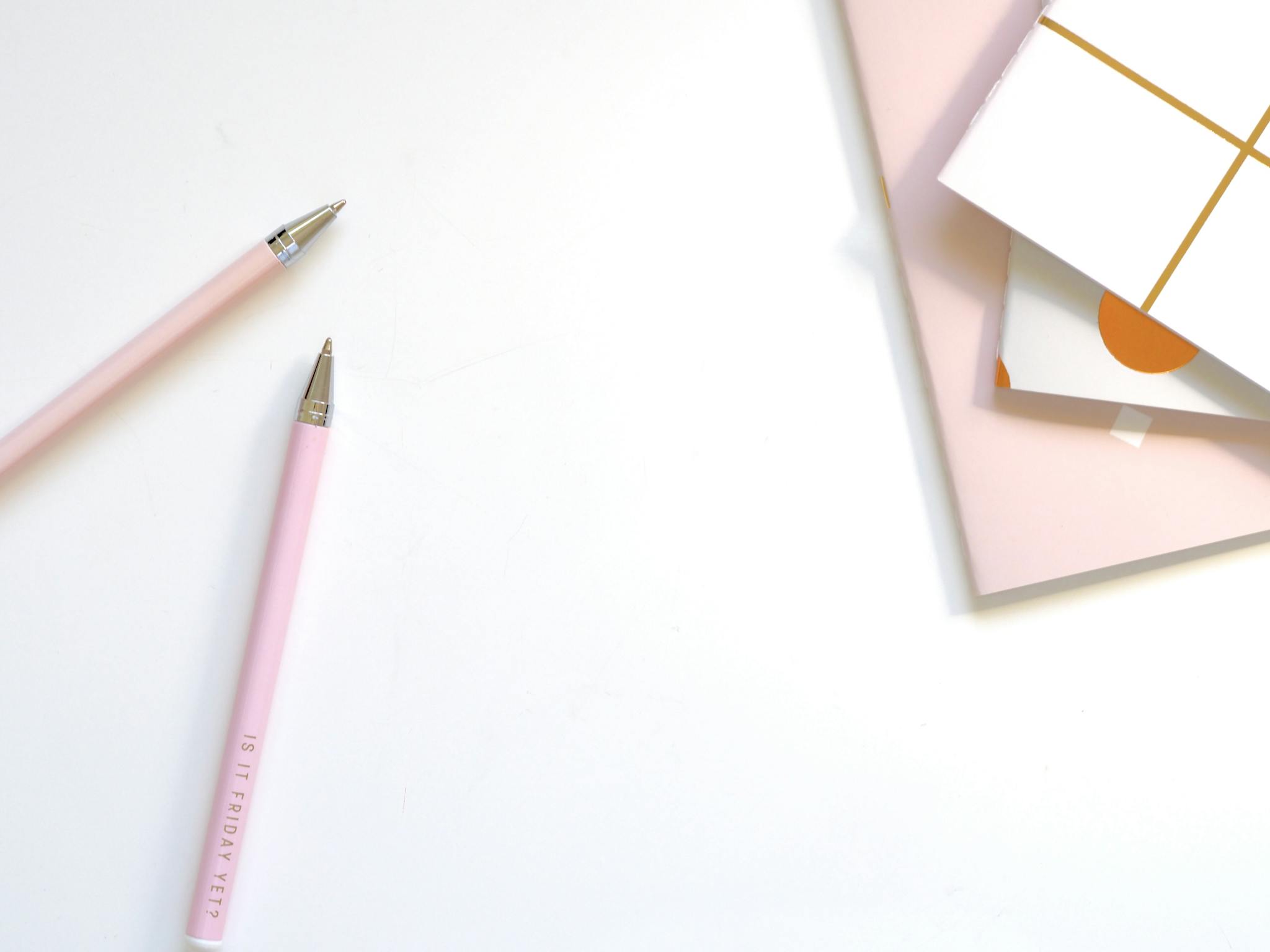 A minimalist flat lay of pink pens and pastel notebooks on a smooth white background, ideal for office and school themes.
