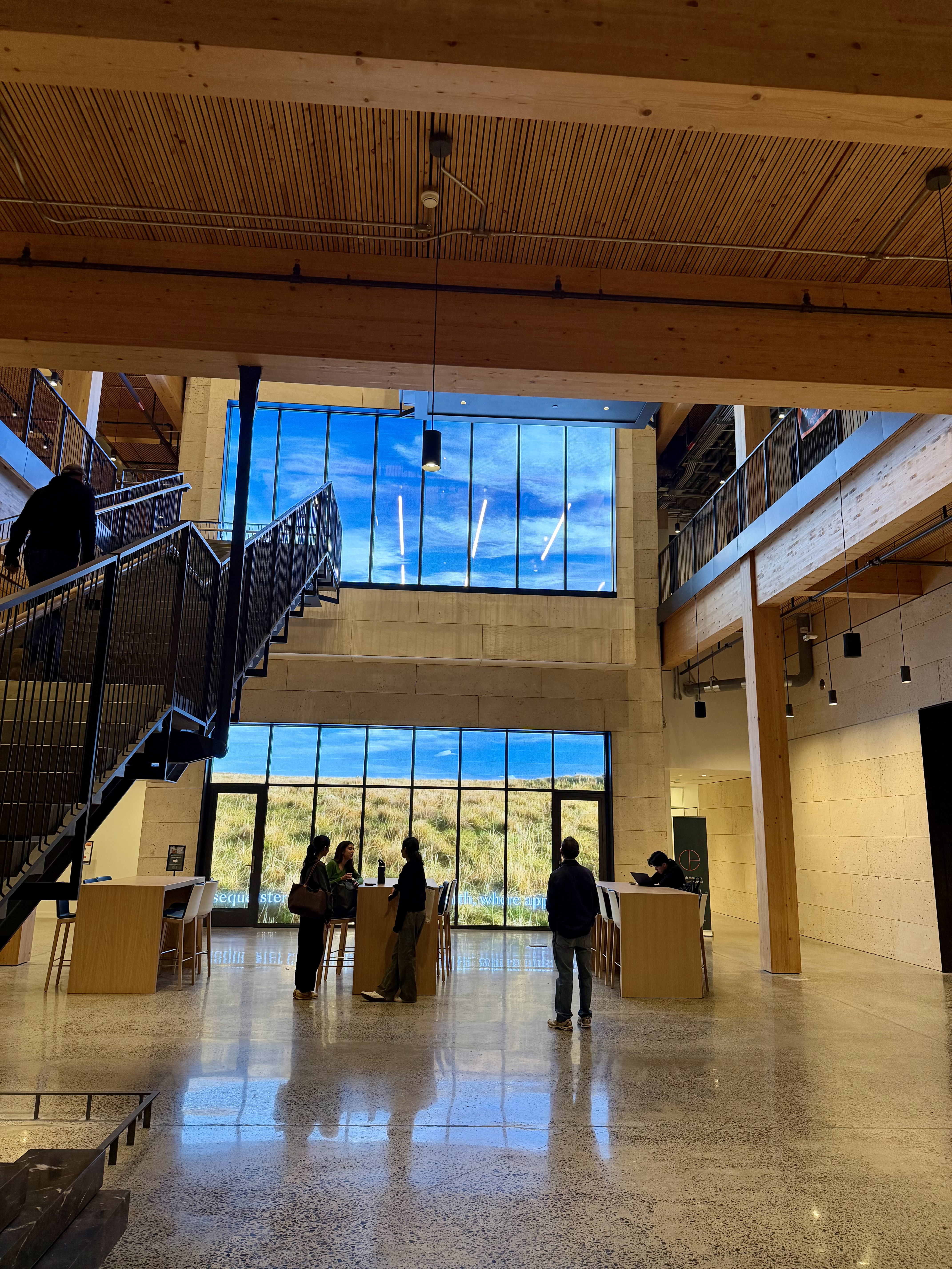 Visitors look at and up toward two large panels showing images of wildlife and a blue sky. A stairway to the second floor is at left.