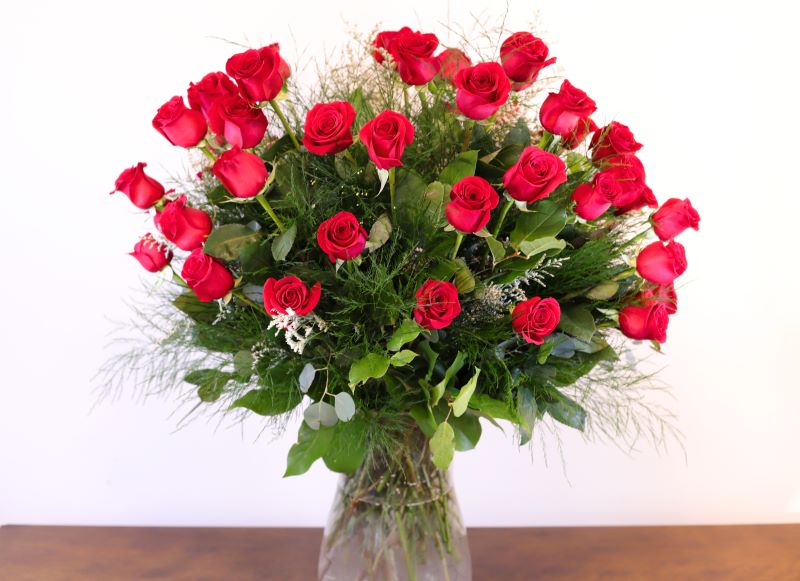 Four dozen long stem red roses with lush foliage in glass vase by Studley Flower Gardens