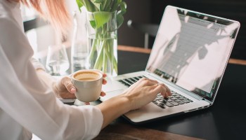 A woman drinking coffee and using a laptop