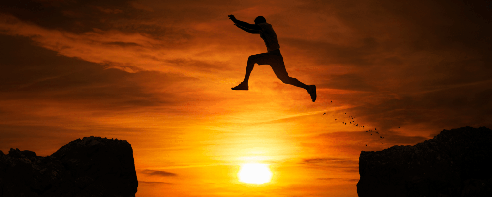Silhouette of a man leaping across cliffs at sunset, symbolizing discipline, resilience, and how to build confidence by facing fear and taking bold action.