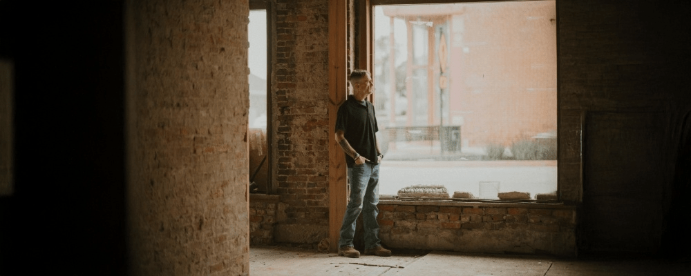 Jim Lunsford stands by a window in an old brick building, looking outside with hands in his pockets.