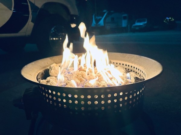Auto-generated description: A portable fire pit with burning flames and glowing rocks is set up outdoors at night, surrounded by parked vehicles.