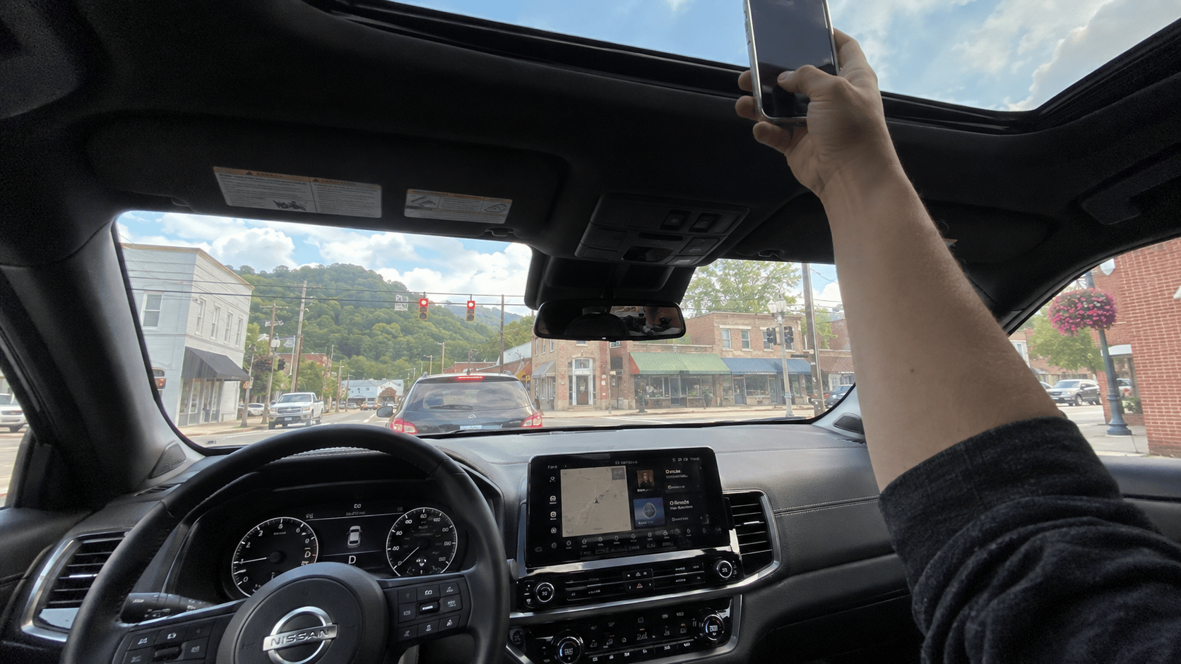 Driver holding a phone up toward the sunroof at a red light in a small Tennessee town, trying to find cell service.
