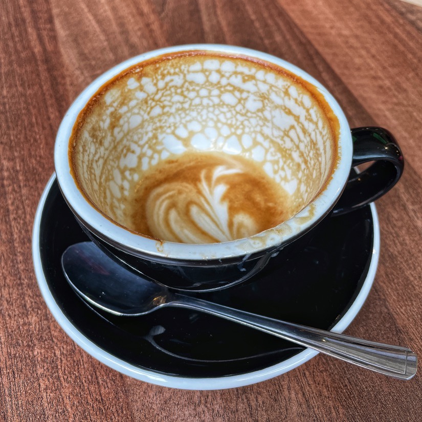 A finished latte in a black cup and saucer, on a table at Monkeyboard Coffee in the the GPO at the Metquarter in Liverpool