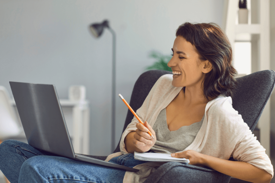 woman working online while smiling and taking notes