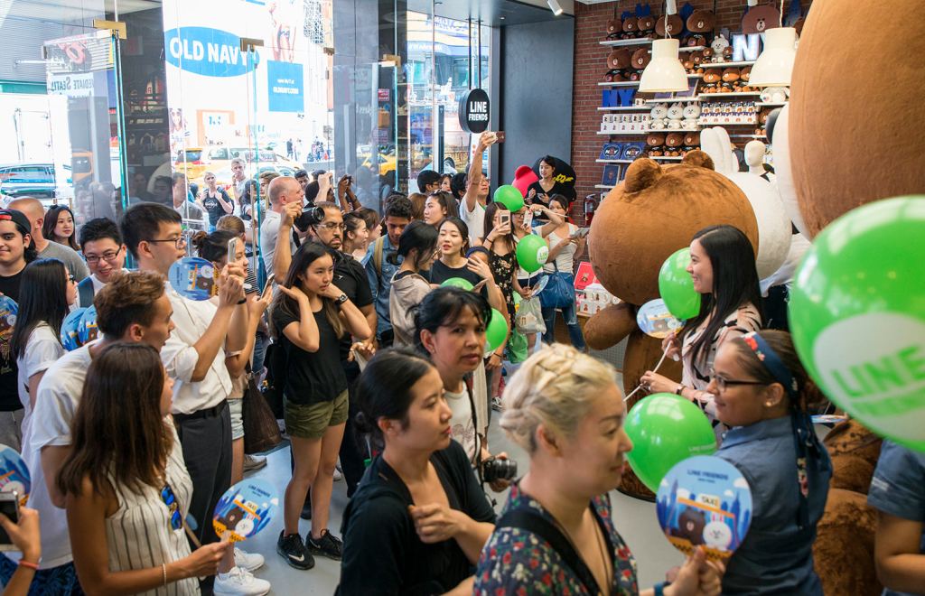 Crowd of shoppers with green balloons and phones around a giant Brown bear plush at a Line Friends store opening