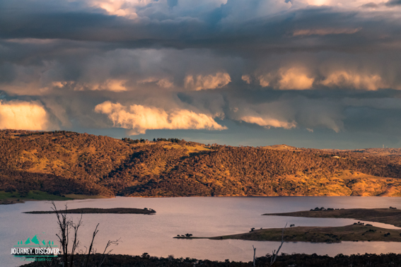 Lake Jindabyne at sunset with dark clouds looming above.