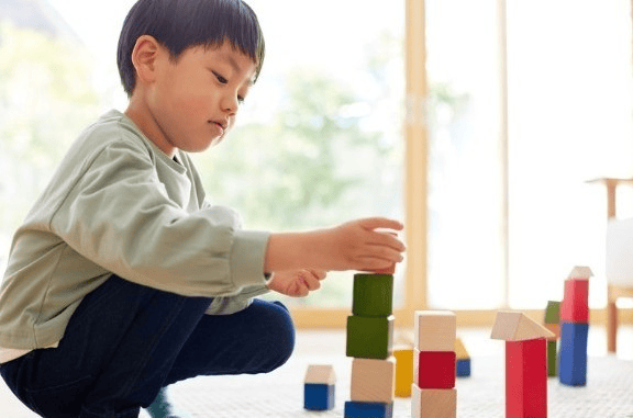 Child sitting on the floor building a tower with colorful wooden blocks in soft natural light.