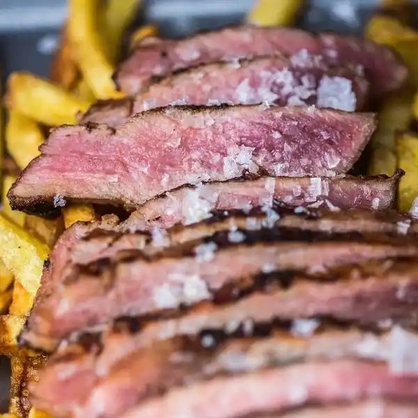 Thickly sliced grilled Pluma Ibérica pork, showcasing a pink center and charred exterior, arranged on a dark wooden board and garnished with fresh rosemary sprigs and coarse sea salt.