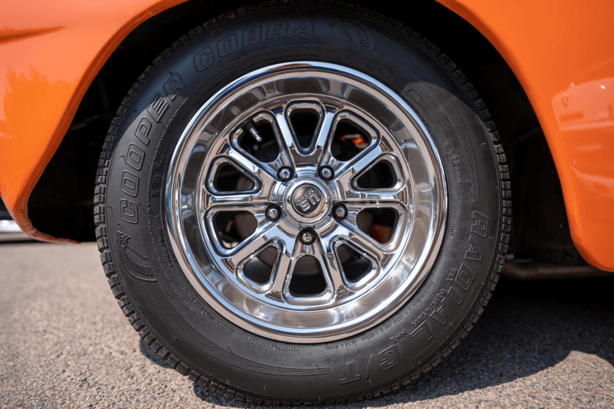 Close-up of a chrome wheel on a classic orange car, showcasing vintage style.