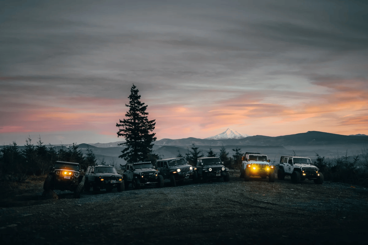 Row of jeeps parked against sunset with mountain backdrop, showcasing adventure and freedom.